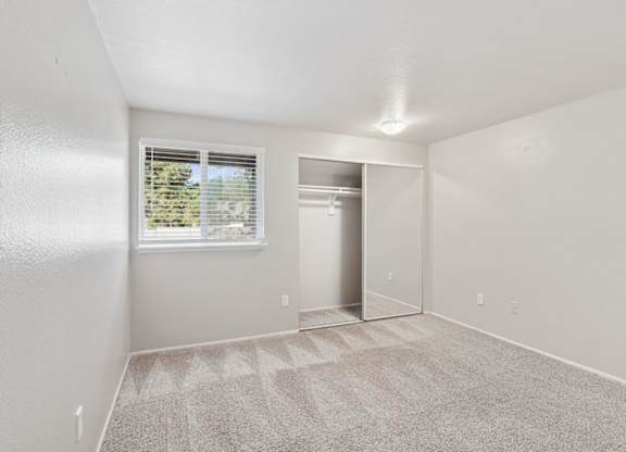 A room with a carpeted floor and a window with blinds.