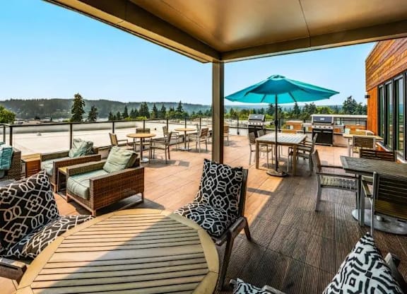 A wooden deck with a blue umbrella and patterned cushions.