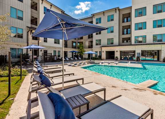 A pool area with sun loungers and umbrellas in front of a building.