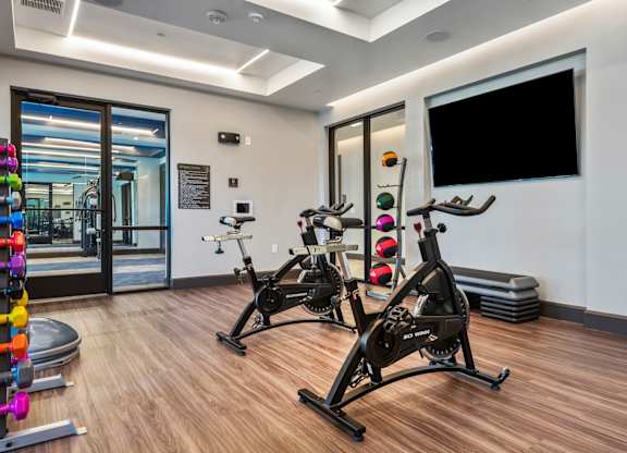 A gym with a row of stationary bikes and a flat screen TV mounted on the wall.