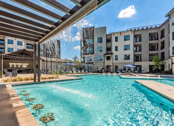 A swimming pool with a waterfall and a building in the background.