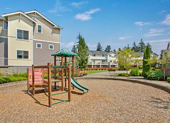 A playground with a green slide and a red swing set in front of apartment buildings.