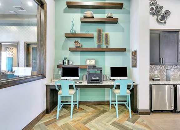 A room with a desk and chairs in front of a wall with shelves and a fridge.