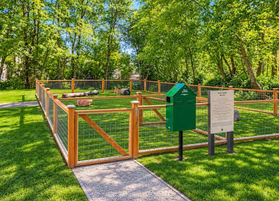 A green trash bin sits next to a sign on a fenced path.