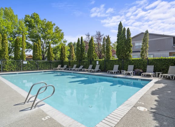 a swimming pool with lounge chairs and trees in the background