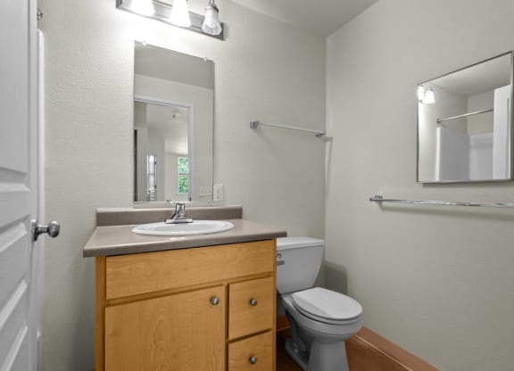 Bathroom with white walls, wooden cabinets, and mirror at Collins Circle apartments in the Goose Hollow district in Portland, Oregon.