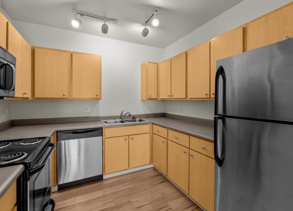 Kitchen with stainless steel appliances, wooden-style flooring, and overhead lighting at Collins Circle apartments in the Goose Hollow district in Portland, Oregon.
