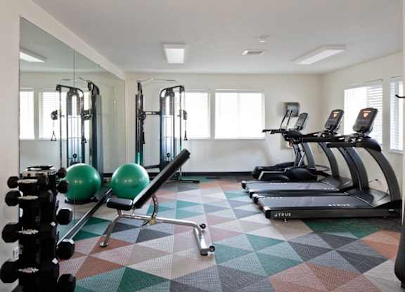 A gym with a variety of equipment including treadmills, weights, and a ball.
