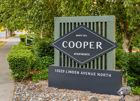 A sign for Cooper Apartments is displayed in front of a tree.