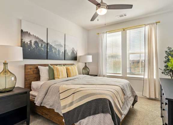 A bedroom with a bed, a ceiling fan, and a painting on the wall.