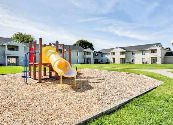A playground with a yellow slide and a red and blue slide in the middle of a gravel area.