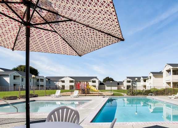 A pool surrounded by chairs and umbrellas with apartment buildings in the background.