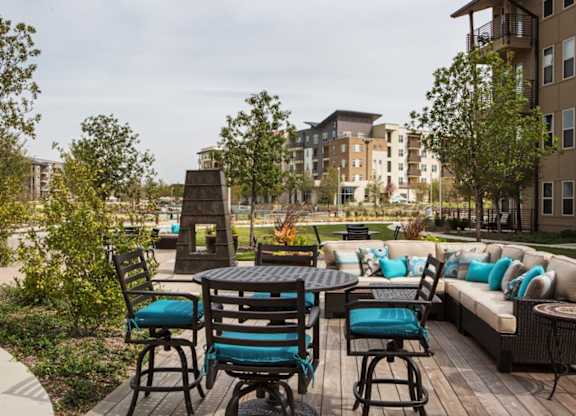 A patio with a table and chairs is surrounded by trees and buildings.