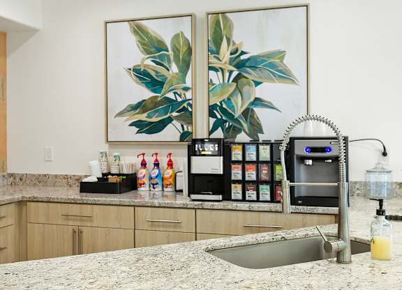 A kitchen with a sink, a fridge, and a painting of a plant on the wall.