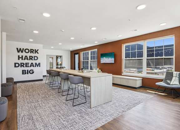 A modern office space with a long table and chairs, a carpeted floor, and a motivational message on the wall.