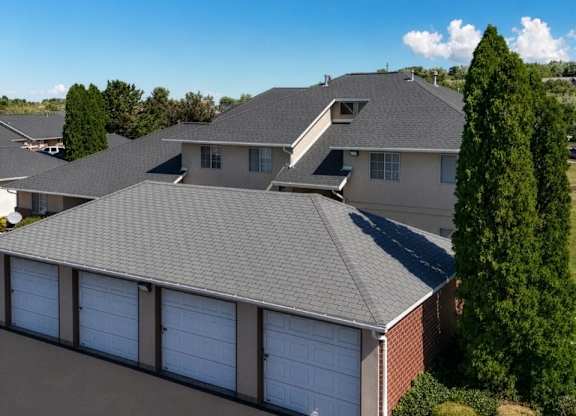 A house with a grey roof and a red flower bed in front.