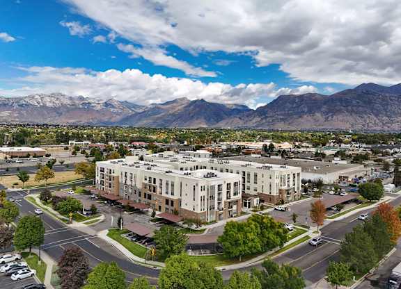 Alvera at the Meadows  large building is surrounded by trees and mountains are in the background.
