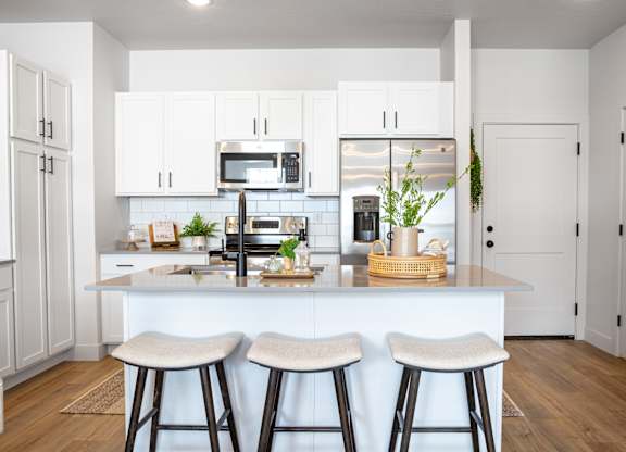 A kitchen with white cabinets and a white island with bar stools.