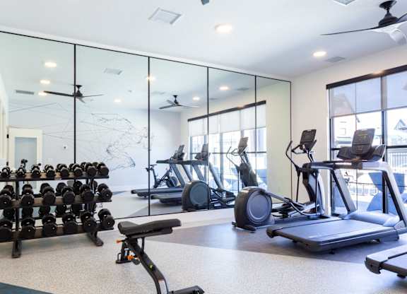 A spacious gym with a variety of equipment including treadmills, stationary bikes, and dumbbells.