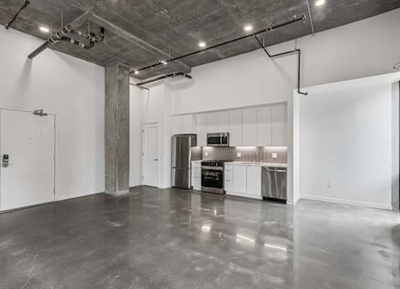 A large empty room with a kitchen area in the background.