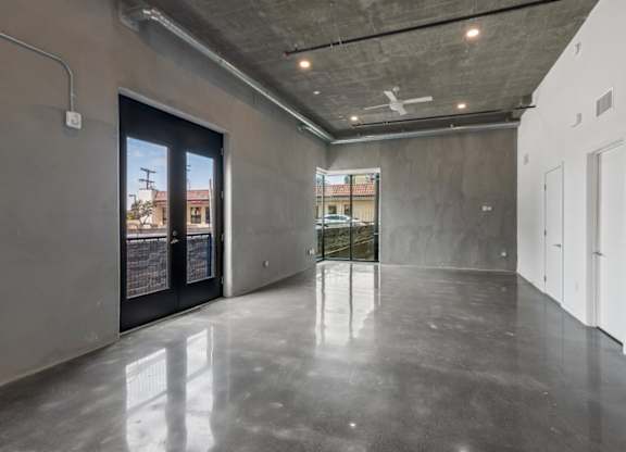 A spacious room with a concrete floor and walls, featuring a large window with a view of the outside.