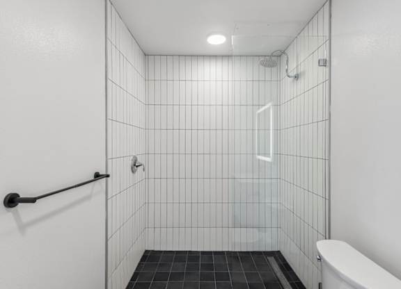 A white tiled bathroom with a toilet and a shower.