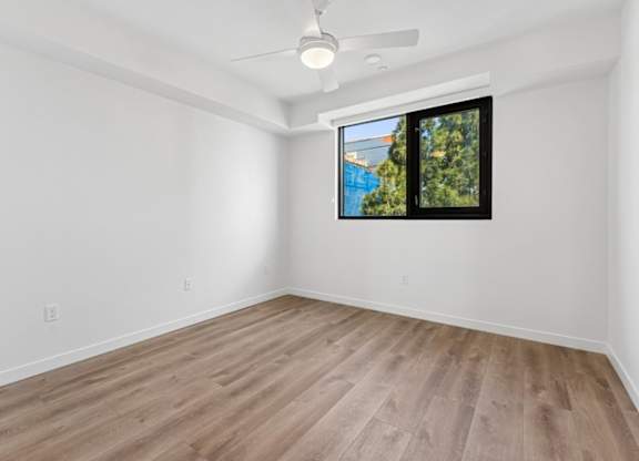 A room with a ceiling fan and a window overlooking a pool and trees.