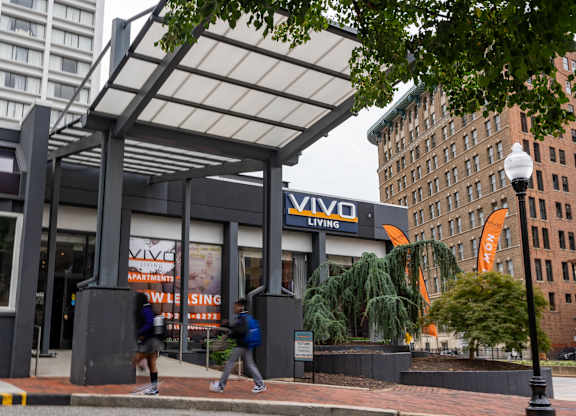 Two people are walking past a building with a sign that says "VIVO".