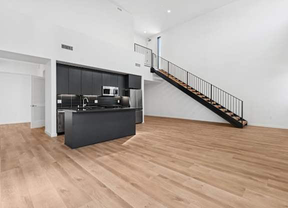A kitchen with a black countertop and a wooden staircase.