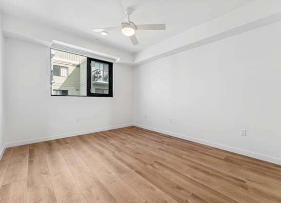 A room with a ceiling fan and a window showing a building outside.