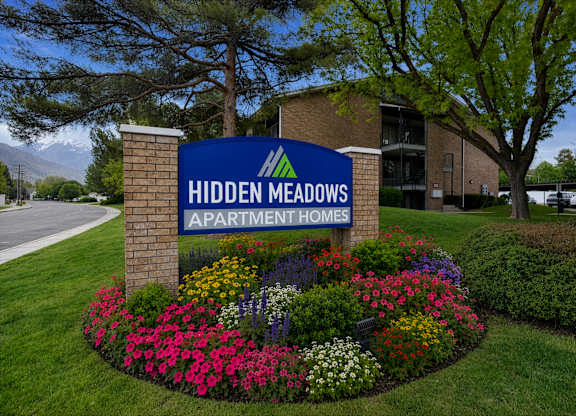 A sign for Hidden Meadows Apartment Homes is surrounded by flowers.