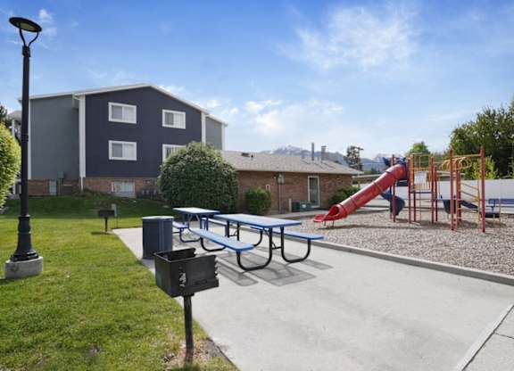 A playground with a slide and a bench in front of a building.