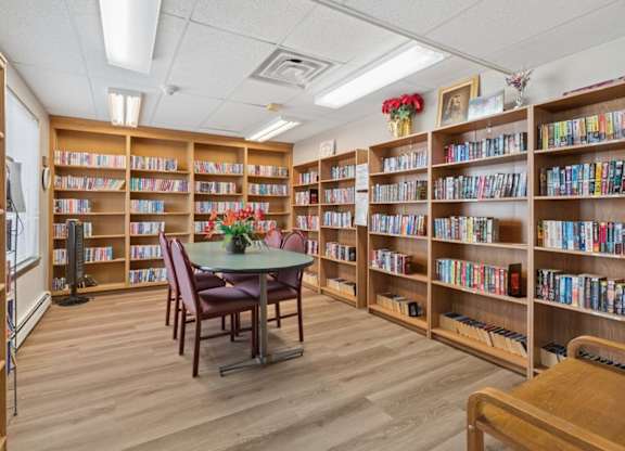 A library with wooden shelves filled with books and a table in the middle.