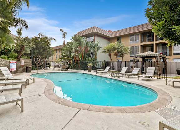 A swimming pool surrounded by lounge chairs and palm trees.