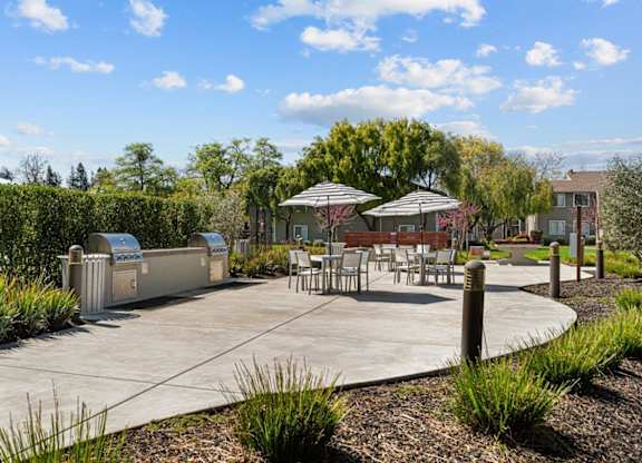 A park with a table and chairs and a trash can.