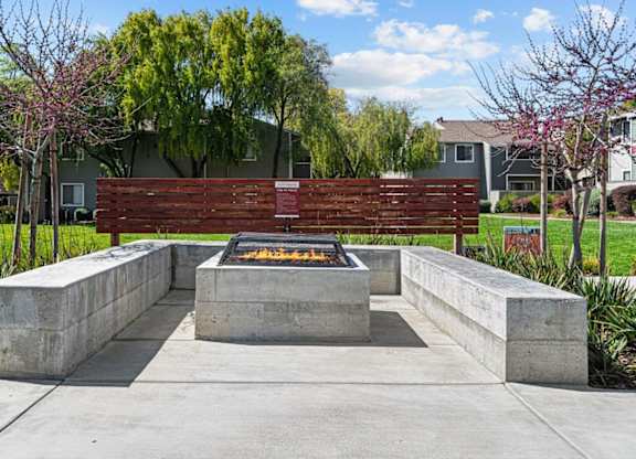 A fire pit is surrounded by concrete blocks in a park.