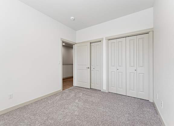 A room with white walls and a carpeted floor with three doors.
