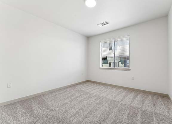 A room with a carpeted floor and a window with blinds.