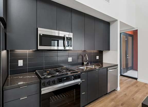 A modern kitchen with dark grey cabinets and a stainless steel stove top.