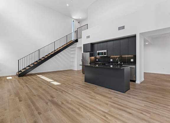 A black staircase with a metal railing leads to a kitchen area.