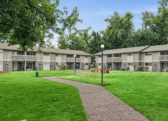 A grassy area with a concrete walkway separates the front of apartment buildings.
