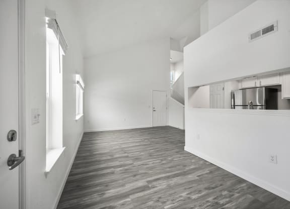an empty living room with a kitchen in the background