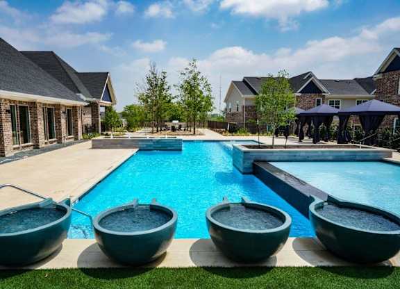 A swimming pool with four bowl-shaped hot tubs lined up on the grass.