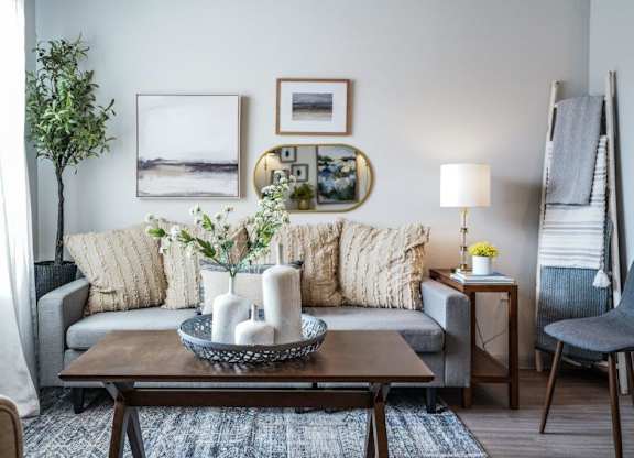 A living room with a grey couch, a coffee table, and a potted plant.