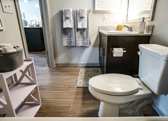 A white toilet sits in a bathroom with a wooden floor and a white sink.