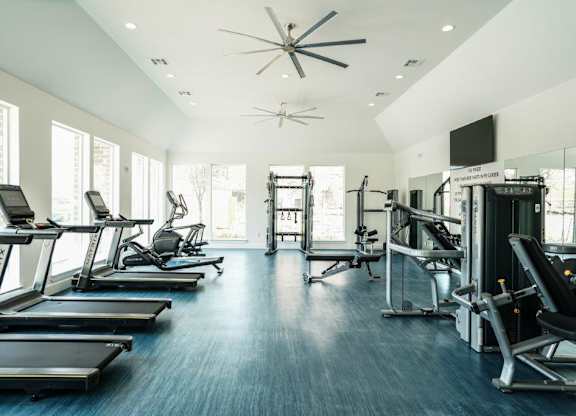 A spacious gym with treadmills, exercise machines, and a ceiling fan.