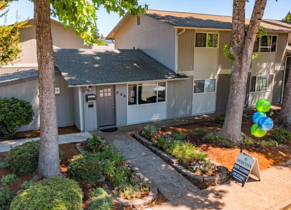 the front of the house with two trees and a sign in the front yard