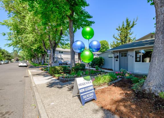 a sidewalk with a sign and balloons in front of a building