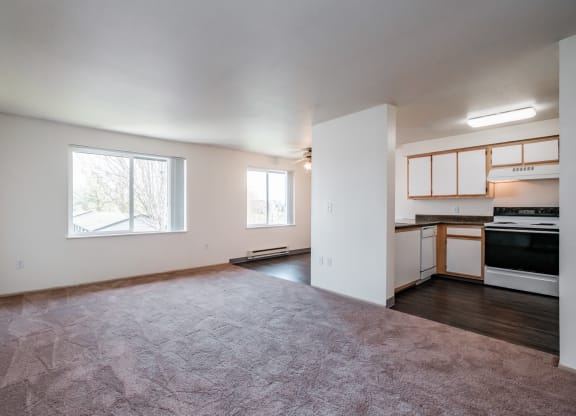 an empty living room with a kitchen in the background