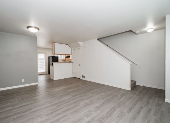 an empty living room with a kitchen in the background